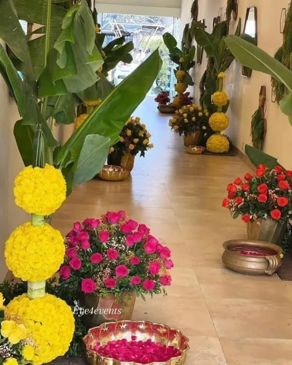 I created this blooming pathway to welcome guests to a festive celebration. The walkway is lined with arrangements of yellow marigold globes, vibrant pink roses in brass pots, and floating petals in urlis.