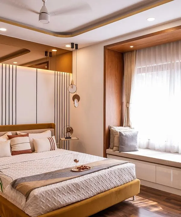 A sophisticated master bedroom featuring a stylish bed with a mustard-colored frame and a chic paneled headboard. The design includes a cozy window seat with built-in storage, perfect for relaxing with a book.