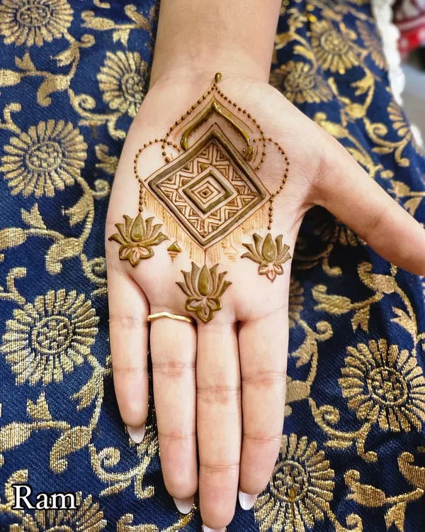 A modern, jewellery-style design for the palm. This pattern features a central geometric element with hanging lotus charms, giving it a delicate look.