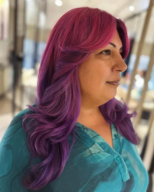 A fun and vibrant look with curtain bangs and face-framing layers. The pink and violet hair color makes a bold statement, and the cut adds beautiful shape.