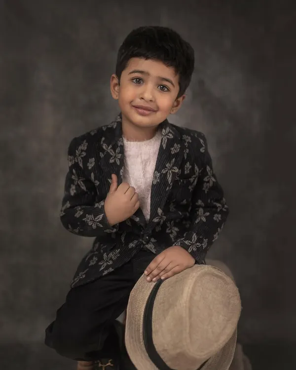 A classic, colored portrait of a young boy in a stylish floral blazer, holding a hat. The painterly backdrop and his gentle expression create a timeless piece of art.