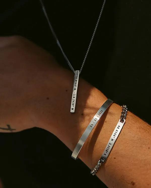 This image showcases a matching set for him, featuring a silver-toned bar necklace and two engraved bracelets. It's a perfect example of how to create a coordinated, personal look.