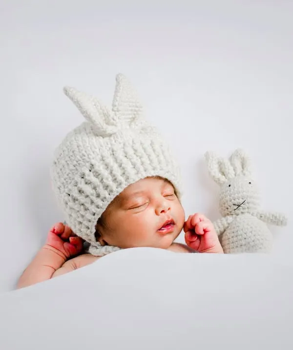 We love creating these adorable themed portraits. This sleeping baby in our hand-knitted bunny hat, complete with a matching toy, is one of our most requested newborn photoshoot setups.