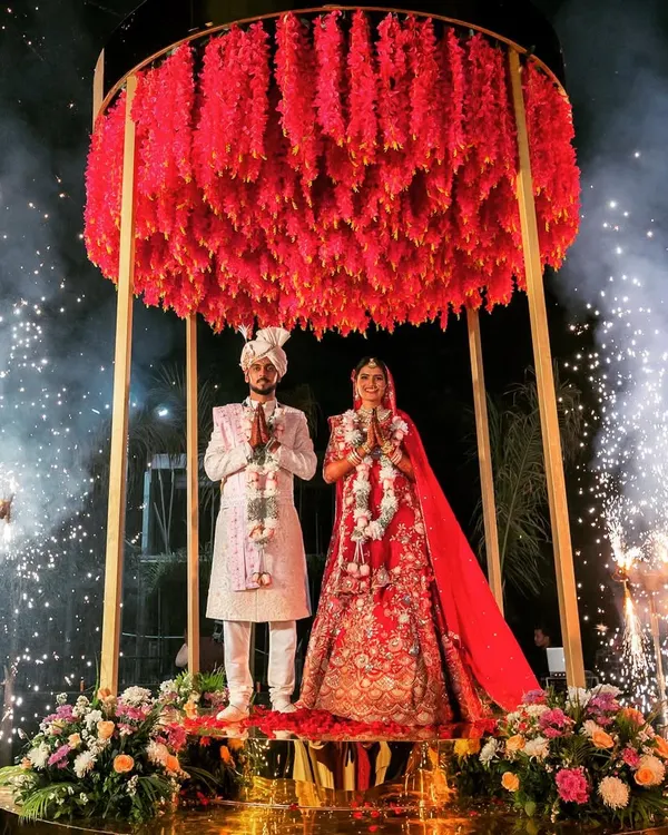 A Varmala that feels like it's floating in the heavens. We designed this elevated circular stage with a dense canopy of red florals, surrounded by cold pyros, to create a truly magical and unforgettable moment for the couple.
