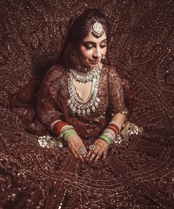 A breathtaking top-down shot of the bride, seated within the magnificent spread of her heavily embroidered wedding lehenga. This artistic angle showcases the grandeur of the bridal attire.