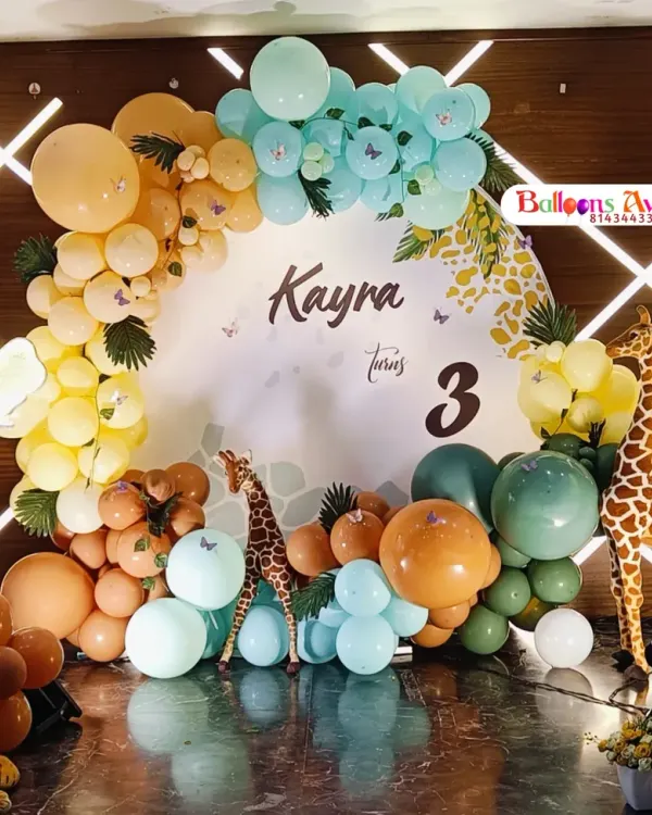 A complete jungle-themed stage for a third birthday party. This setup features a custom circular backdrop, a colorful balloon arch, and a variety of realistic animal props like a lion, giraffe, and zebra to create an immersive safari experience.