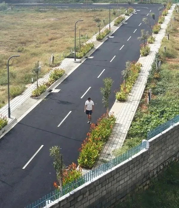 An aerial view of our completed BTM Meadows layout, showing the clean geometry of the asphalt road, paved sidewalks, and regularly spaced streetlights. The planted medians with young trees and shrubs are designed to mature into a green canopy over time.