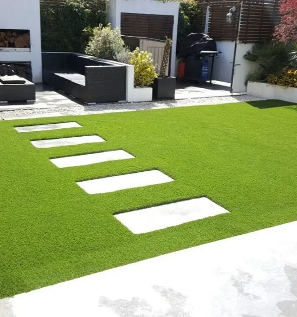 This modern patio design features clean lines with rectangular stone pavers set into a field of vibrant artificial grass. It creates a sophisticated and practical outdoor lounge area that is always ready for guests.