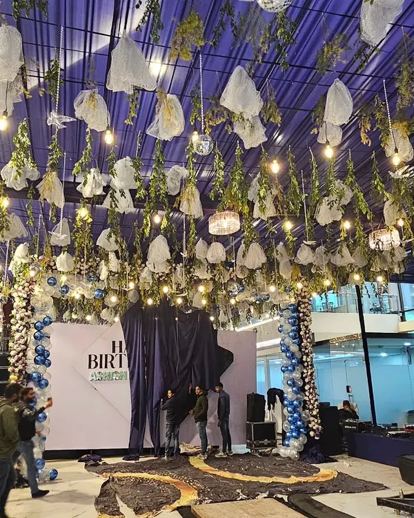 A full view of a massive birthday party decoration I executed. The ceiling is covered in blue fabric, with hanging greenery, lights, and disco balls to create a magical, starry night theme.