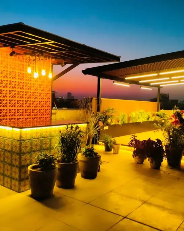 A stunning custom bar on a Gurgaon terrace, featuring a backlit patterned tile front and a terracotta jaali screen. The warm lighting creates an inviting atmosphere for evening drinks.