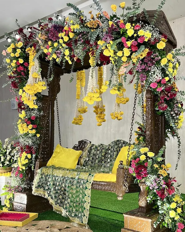A stunning Haldi swing setup, overflowing with colorful flowers. We used a traditional wooden swing and decorated it with a mix of yellow, pink, and red blooms, along with hanging floral strings for a festive look.