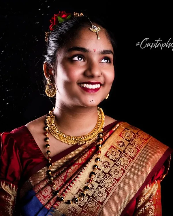 A joyful portrait of a model in a traditional Marathi-style saree. The studio lighting is set to highlight the rich colours of the fabric and the intricate gold jewellery, creating a warm and celebratory image.