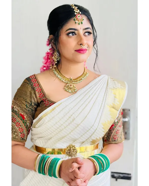 A classic South Indian bridal look with a white and gold saree, temple jewelry, and jasmine flowers. This is a perfect reference for a traditional wedding music performance.