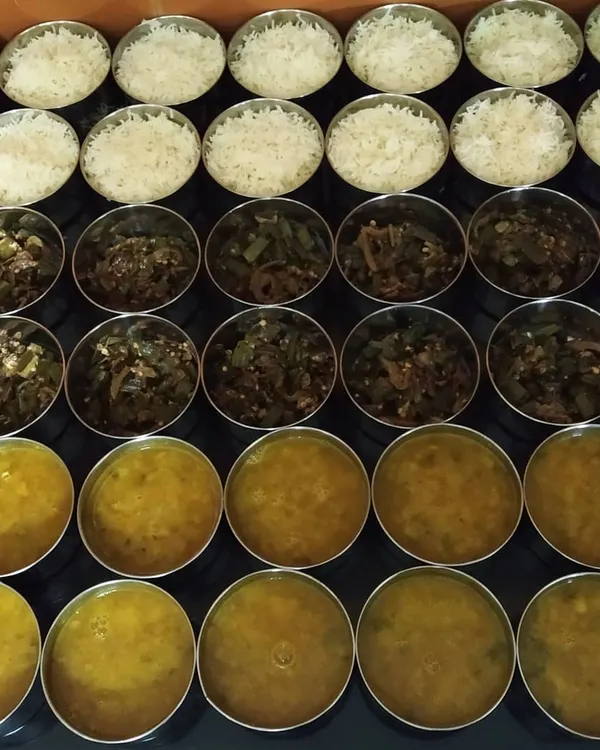 Preparing a bulk order of tiffins for an office in Greater Noida. Each component, from the bhindi sabzi to the dal and rice, is portioned carefully to ensure everyone gets a perfect meal.