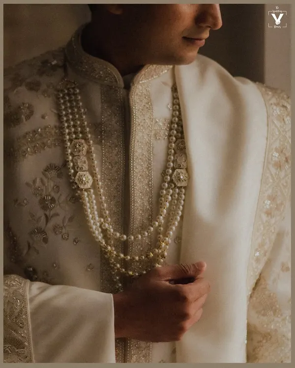 A close-up shot of the groom's royal attire, focusing on the intricate pearl necklaces and the fine embroidery of his sherwani. This detail shot speaks of elegance and tradition.