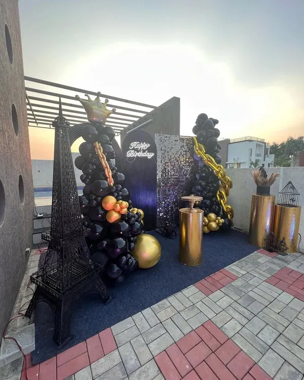 A complete view of the stylish black and gold rooftop party, featuring a miniature Eiffel Tower, balloon Christmas trees with gold chains, and a sequin backdrop.