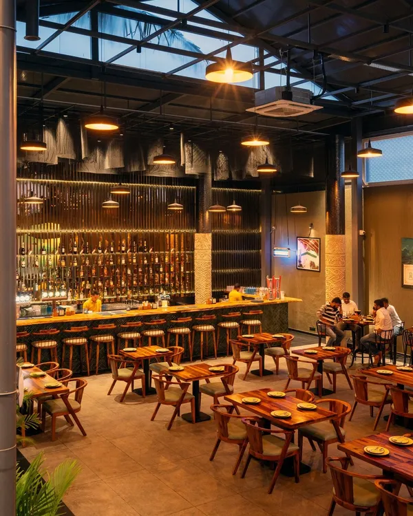 Welcome to Pincode 24, a 7500 sq ft restobar in Hebbal, Bengaluru. This view captures the essence of our industrial chic design, where the grand, glossy bar serves as the focal point. We balanced the raw energy of the exposed steel grid ceiling and concrete-texture floors with the warmth of custom wooden furniture and layered, versatile lighting.