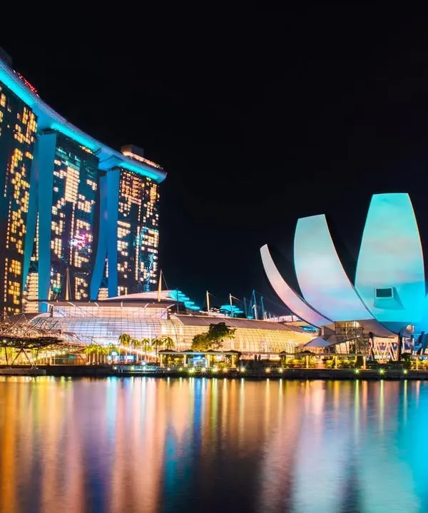 The iconic Marina Bay Sands and ArtScience Museum in Singapore are brilliantly lit in blue and white, their reflections shimmering on the water at night.