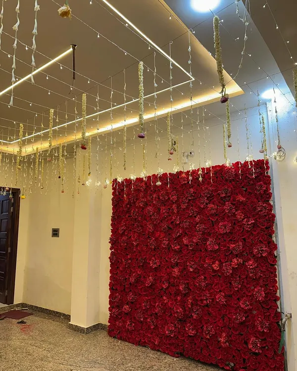 A magnificent red rose flower wall, perfect as a photo backdrop for a wedding, engagement, or any glamorous event. The hanging floral strings from the ceiling add an extra layer of detail.