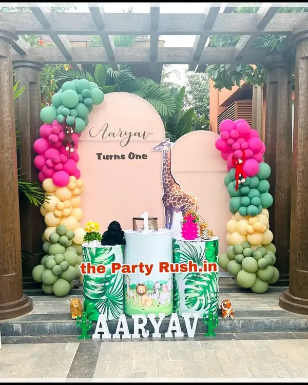 This outdoor jungle theme for Aaryav's first birthday shows how I can integrate elaborate setups into natural surroundings. The decor features vibrant balloon garlands, a giraffe cutout, and themed pedestals, all framed by a beautiful garden structure.