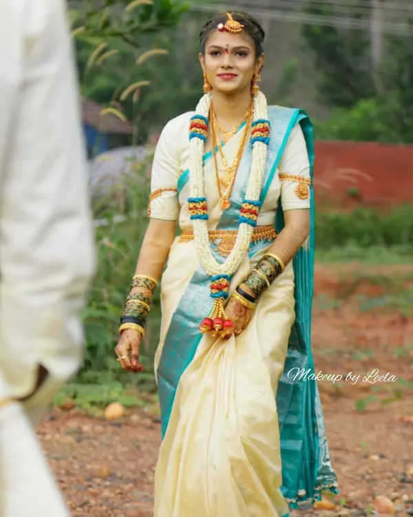 A radiant South Indian bride ready for her Muhurtham. This look features classic makeup that enhances her natural beauty, paired with a traditional off-white and teal silk saree and authentic temple jewelry.