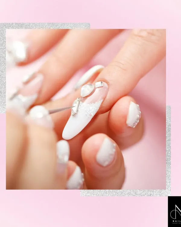 Mastering precision is key. This image shows the application of white gel polish and silver heart-shaped gems, a technique covered in our advanced nail art module for creating detailed bridal and special occasion looks.