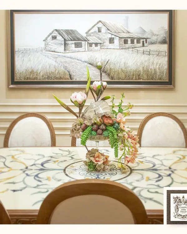 This dining setting showcases a classic marble inlay table, where each piece is carefully placed to create a harmonious design. The elegant floral centerpiece and rustic farmhouse wall art complete this picture of refined country living.