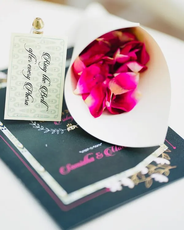 A close-up of the personalized details from a minimalist wedding. Each guest's seat had a custom program, a paper cone filled with fresh rose petals, and a small tag with a bell, inviting them to participate in the ceremony.