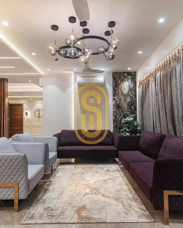 A view of a luxurious living room we designed, featuring a plush purple and grey sofa combination. The space is anchored by a modern statement chandelier and gold accents, creating an atmosphere of sophisticated comfort perfect for entertaining.