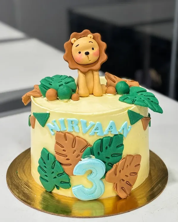 A sweet jungle-themed cake for Nirvaan's 3rd birthday. This design features a cute, handmade fondant lion topper, monstera leaves, and a personalized name banner.