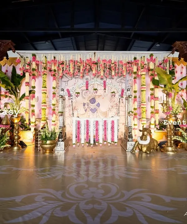 A wide view of the magnificent stage for Dhanvith's naming ceremony. The design incorporates carved wooden pillars, intricate floral arrangements, and a custom floor decal to create a complete, immersive, and traditional experience.