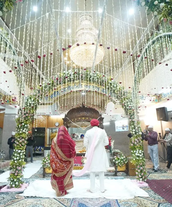 A wide-angle view of the Anand Karaj ceremony, showing the beautifully decorated Gurudwara and the couple taking their laavan. This shot captures the spiritual atmosphere of a Sikh wedding.