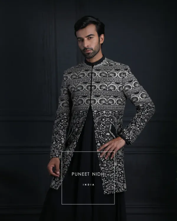 A structured black Achkan layered over a kurta, defined by a mandarin collar and sleek lines. Intricate silver embroidery cascades upward in floral and geometric patterns, offering a perfect fusion of tradition and contemporary style.