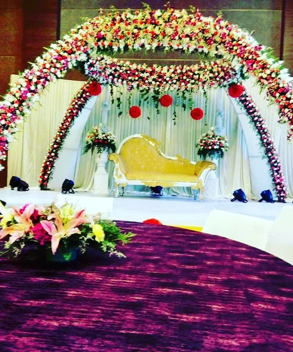 A full view of one of our grand stage designs, perfect for a wedding reception or anniversary. The combination of a dense floral arch, a classic chaise lounge, and strategic lighting creates a truly regal setting.