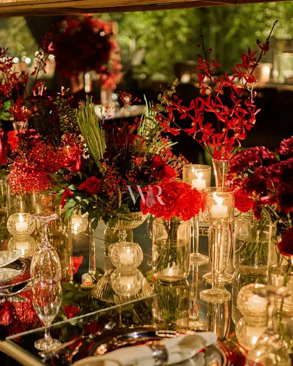 A close-up of a mirrored tablescape, where a runner of red orchids and roses is reflected beautifully. The crystal glassware and silver charger plates add to the layers of luxury and refinement.