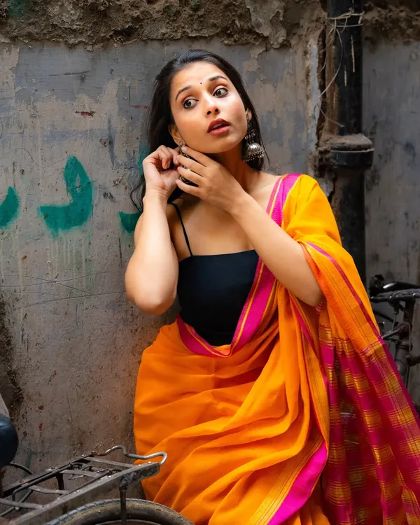 A candid moment in a quiet Delhi alley. The bright orange and pink saree pops against the weathered walls, creating a beautiful, spontaneous portrait.