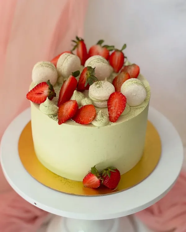 A beautiful matcha and strawberry cake. The light green matcha-infused buttercream is perfectly complemented by a generous topping of fresh, juicy strawberries and macarons.