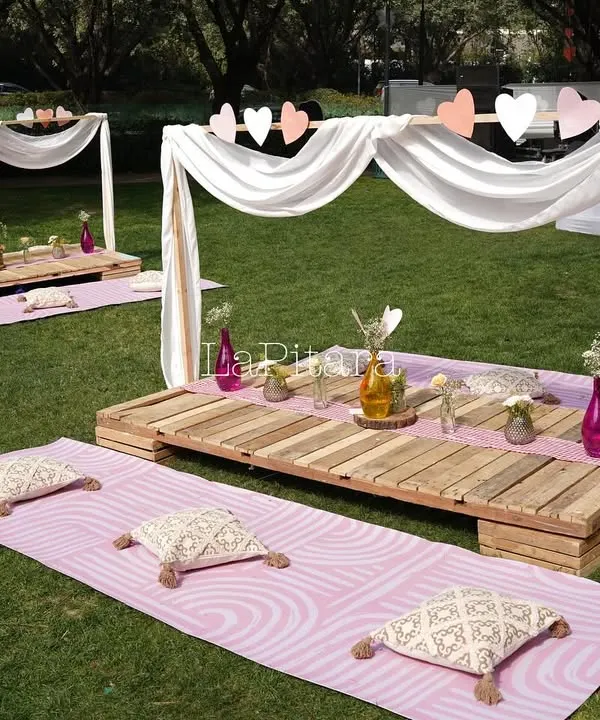 A charming low-seating picnic setup for a Valentine's brunch. We used wooden pallets as tables, surrounded by comfortable cushions on pink mats and framed by a simple white canopy draped with hearts.