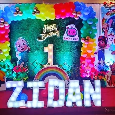 A fun and colorful Cocomelon-themed first birthday party decoration. We used a balloon arch, character cutouts, and large marquee letters spelling out the birthday boy's name, Zidan.