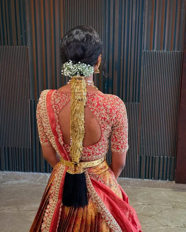 A detailed back view of a traditional South Indian bridal braid, adorned with a golden accessory and fresh baby's breath.