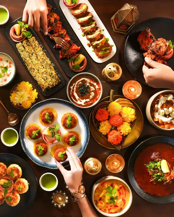 A vibrant Diwali feast captured from above, showing a table full of delicious Indian dishes. This top-down shot highlights the joy of sharing food, with hands reaching in to create a dynamic and inviting scene perfect for festive restaurant promotions.