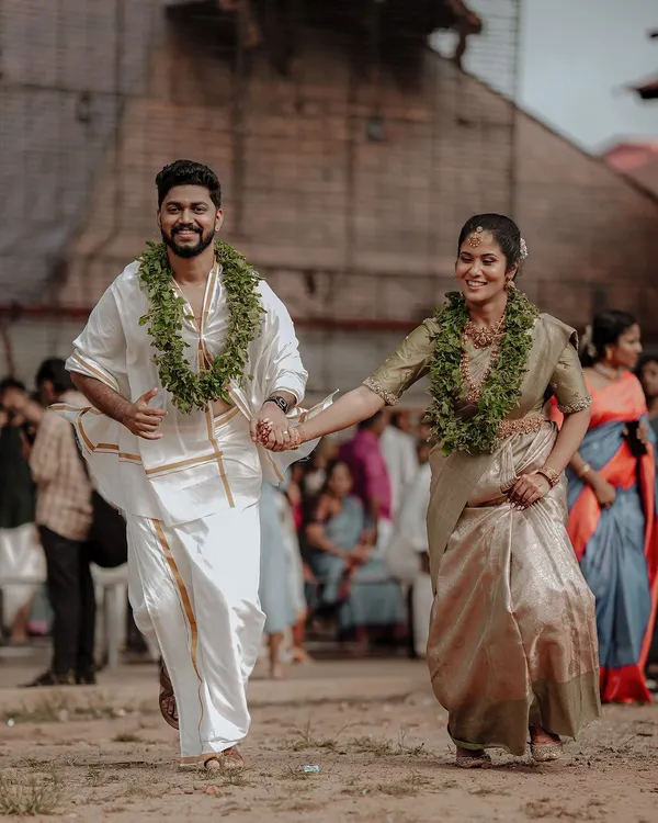 A classic shot of a newly married Kerala couple, hand in hand, walking away from their temple ceremony. Their happy faces and traditional attire tell a story of new beginnings.