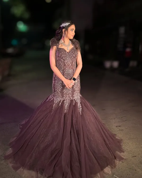 This deep wine-colored fish-cut gown with feather details and intricate beadwork is the definition of glamour. It features a long, dramatic trail for a red-carpet-worthy entrance.