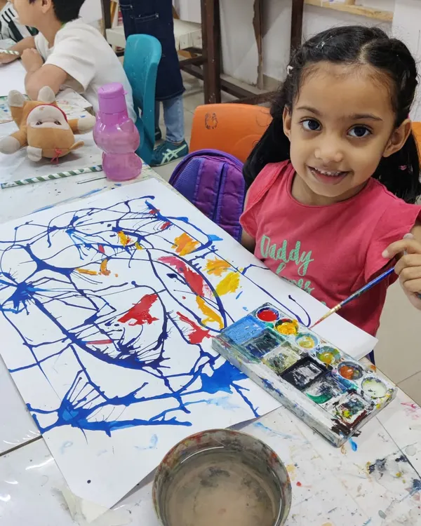 A very young artist smiles for the camera, delighted with her colorful abstract splatter painting. We believe in making art fun and accessible for all ages.