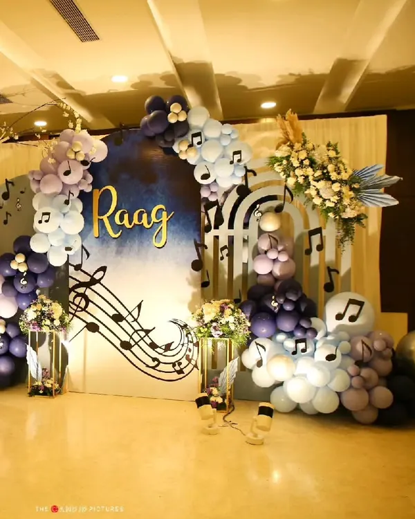 For a naming ceremony celebrating a baby named 'Raag', I designed this music-themed backdrop. It features a cascade of purple and blue balloons, musical notes, and a custom name sign to create a harmonious and joyful setting.