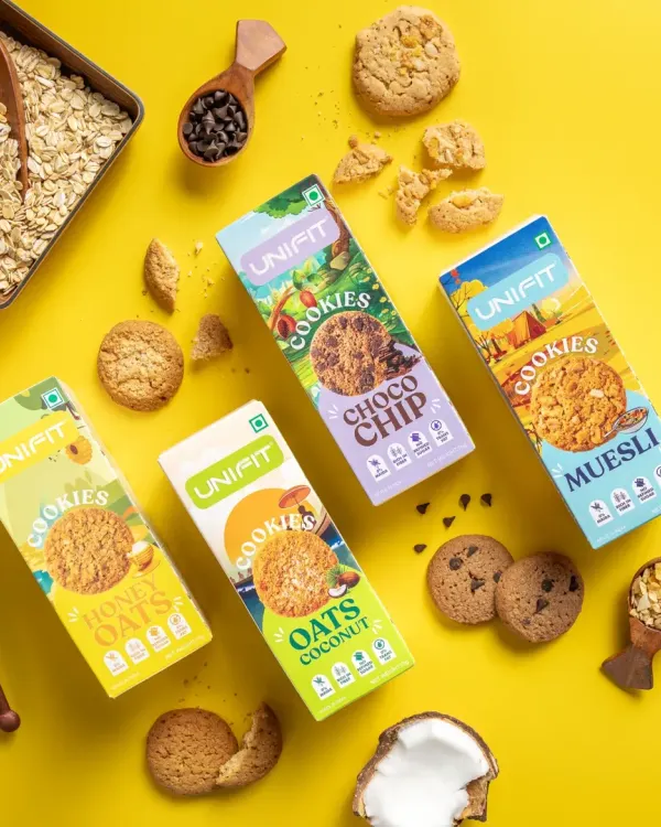 A flat lay of Unifit's cookie range, showcasing four different packaging designs along with their corresponding ingredients like oats, honey, and coconut.