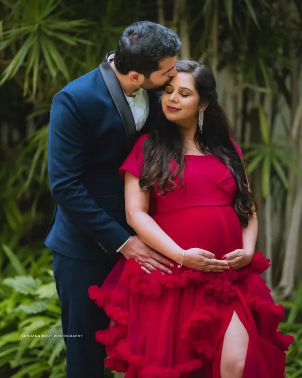 A tender moment captured during an outdoor maternity shoot. The vibrant red gown adds a touch of glamour, while the focus remains on the couple's loving connection.