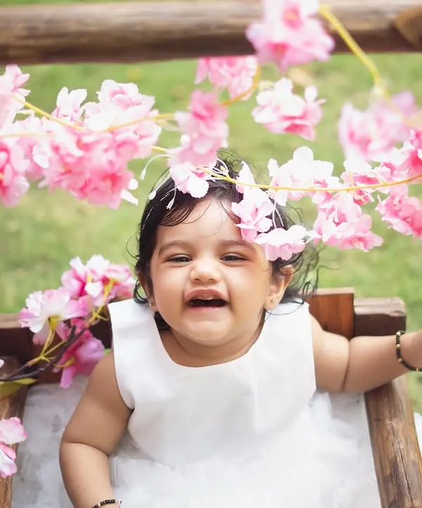 Pure, uninhibited laughter. This little girl is having the best time on a floral swing during her outdoor first birthday shoot. The natural light and greenery create a beautiful, vibrant setting.