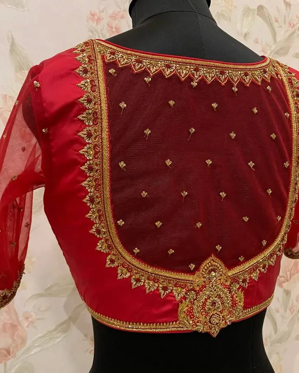 This red blouse features a classic U-shaped back design, framed with heavy zardosi embroidery on a sheer net panel for a regal and elegant look.