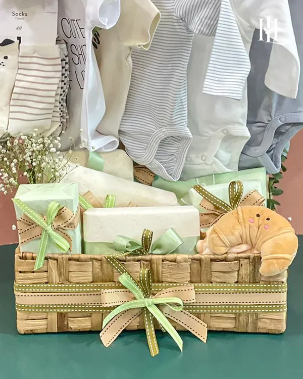 This charming hamper is packed in a woven jute basket and filled with soft, neutral-toned baby clothes and essentials. The plush croissant toy adds a touch of whimsy.
